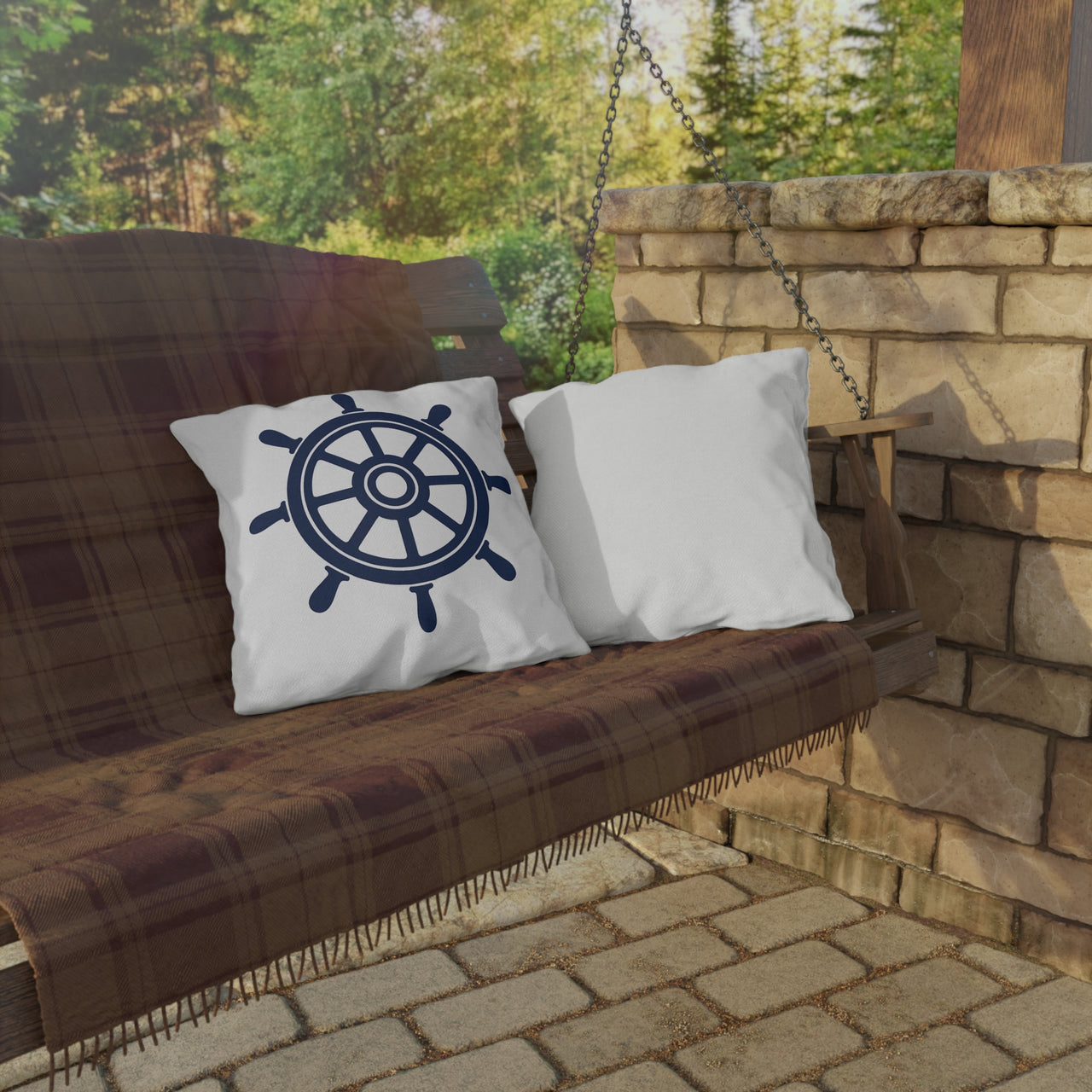 Wooden swing with plaid blanket and pillows, one featuring a ship's wheel design, against a stone wall and greenery.