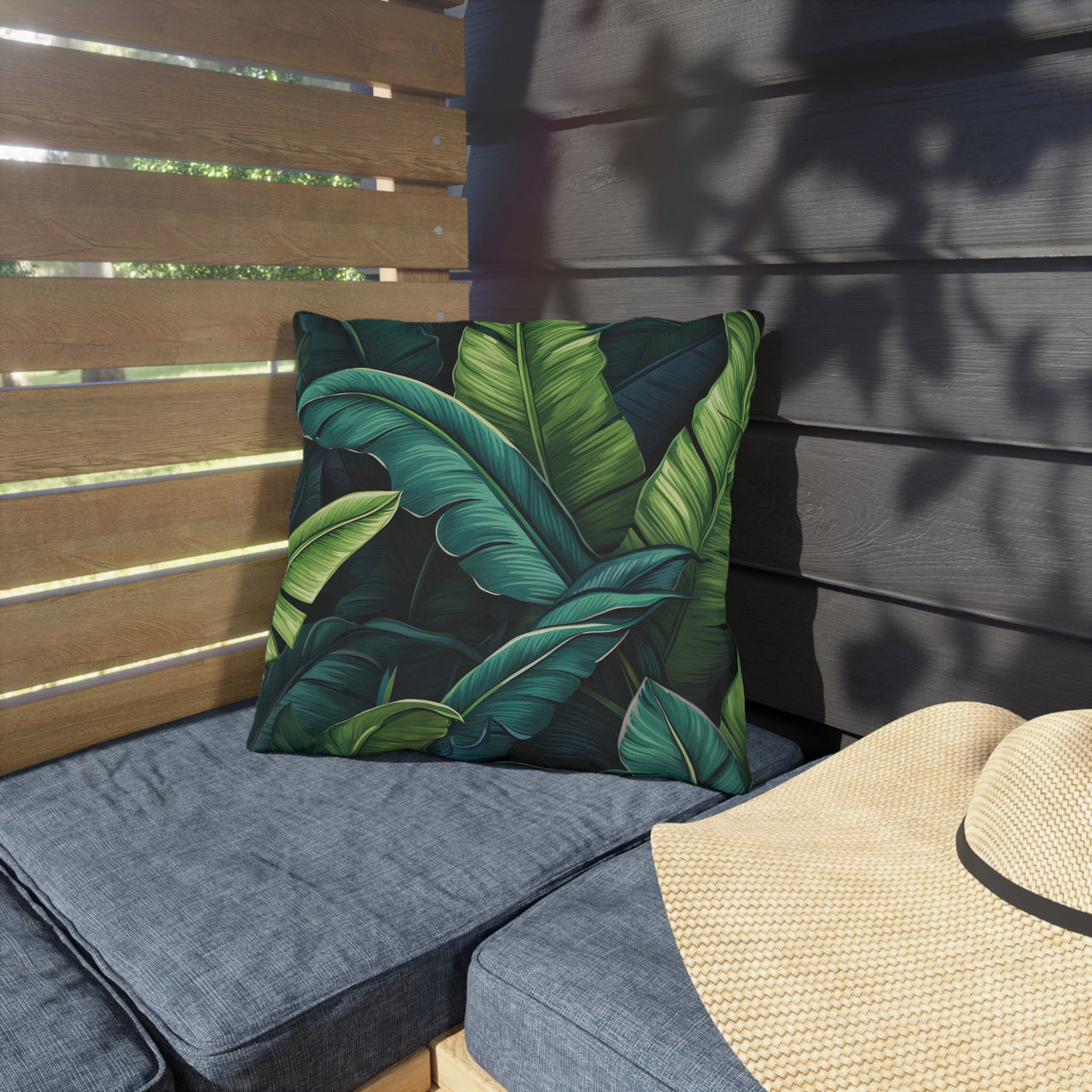 Outdoor seating area with a green leaf-patterned pillow and a straw hat on a wooden bench.